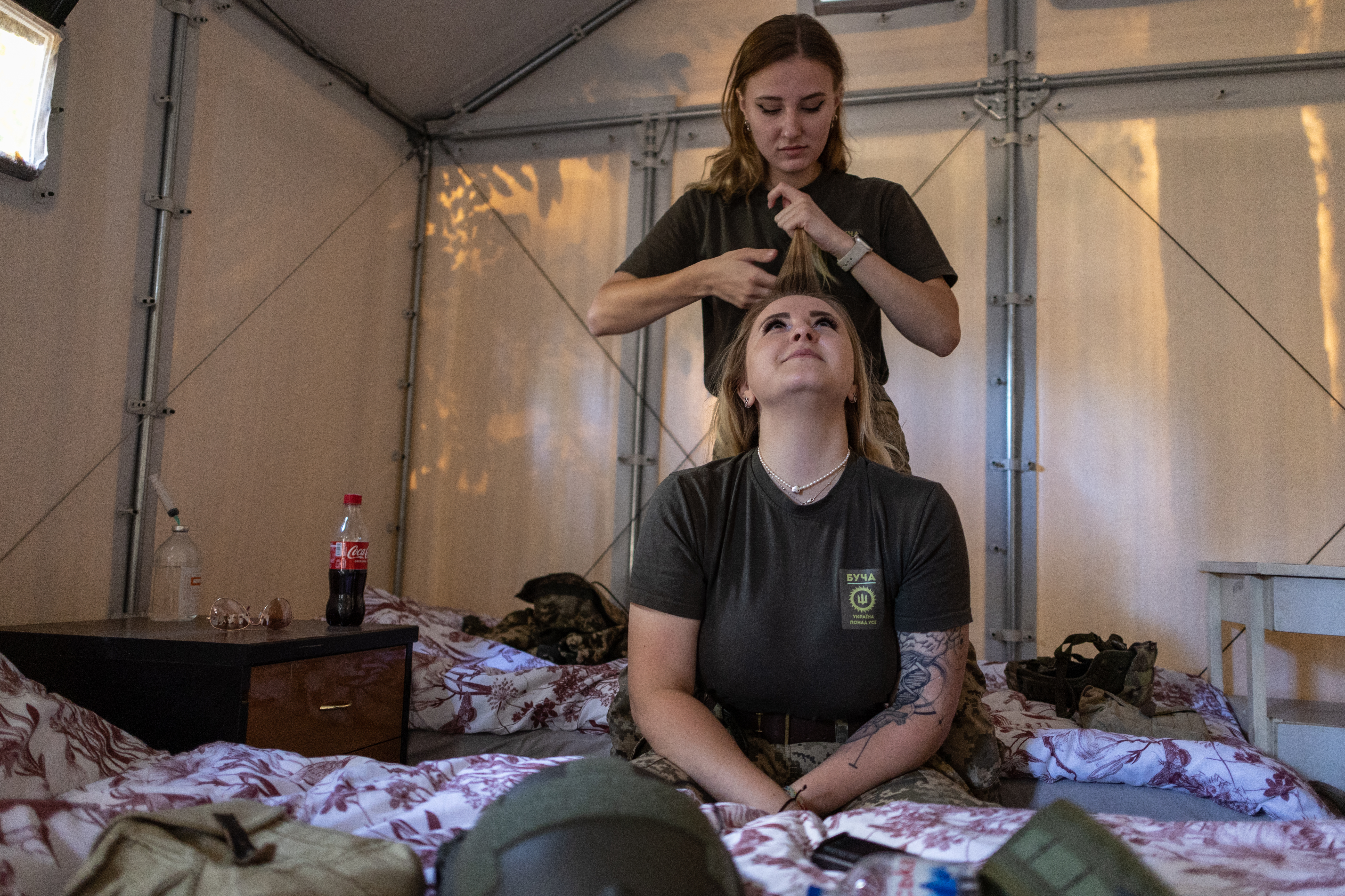 Während ihrer mehrtägigen Einsätze wohnen die Frauen in Zeltlagern im Wald. „Mala“ flechtet ihrer Kameradin „Forsash“ die Haare, um sie unterm Helm zu verstecken. Foto © Andrii Dubtschak/Frontliner 