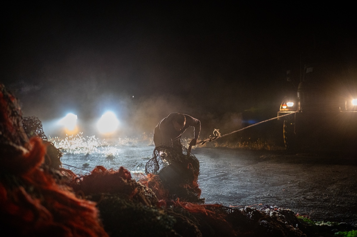 Helfer und Soldaten entladen den Fischernetz-Transport nachts in einem frontnahen Dorf in der Region Charkiw. Foto © Artem Derkatschow/Frontliner